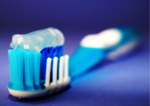 primer plano de cepillo dental con cerdas blancas, celestes y azules y pasta dental blanca. Fondo azul. Cepillarse los dientes