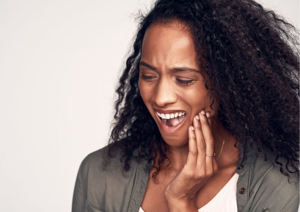 Mujer afroamericana se toca la mejilla con gesto de dolor. Tema: Cuánto tarda una caries en destruir un diente
