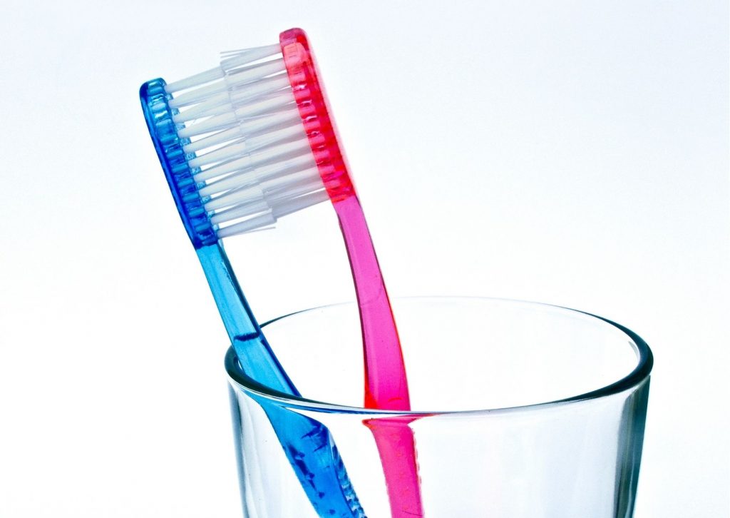 dos cepillos de dientes en un vaso de vidrio, uno azul y otros rojo, tocándose en las cerdas, como si se estuvieran besando. La gingivitis es contagiosa.