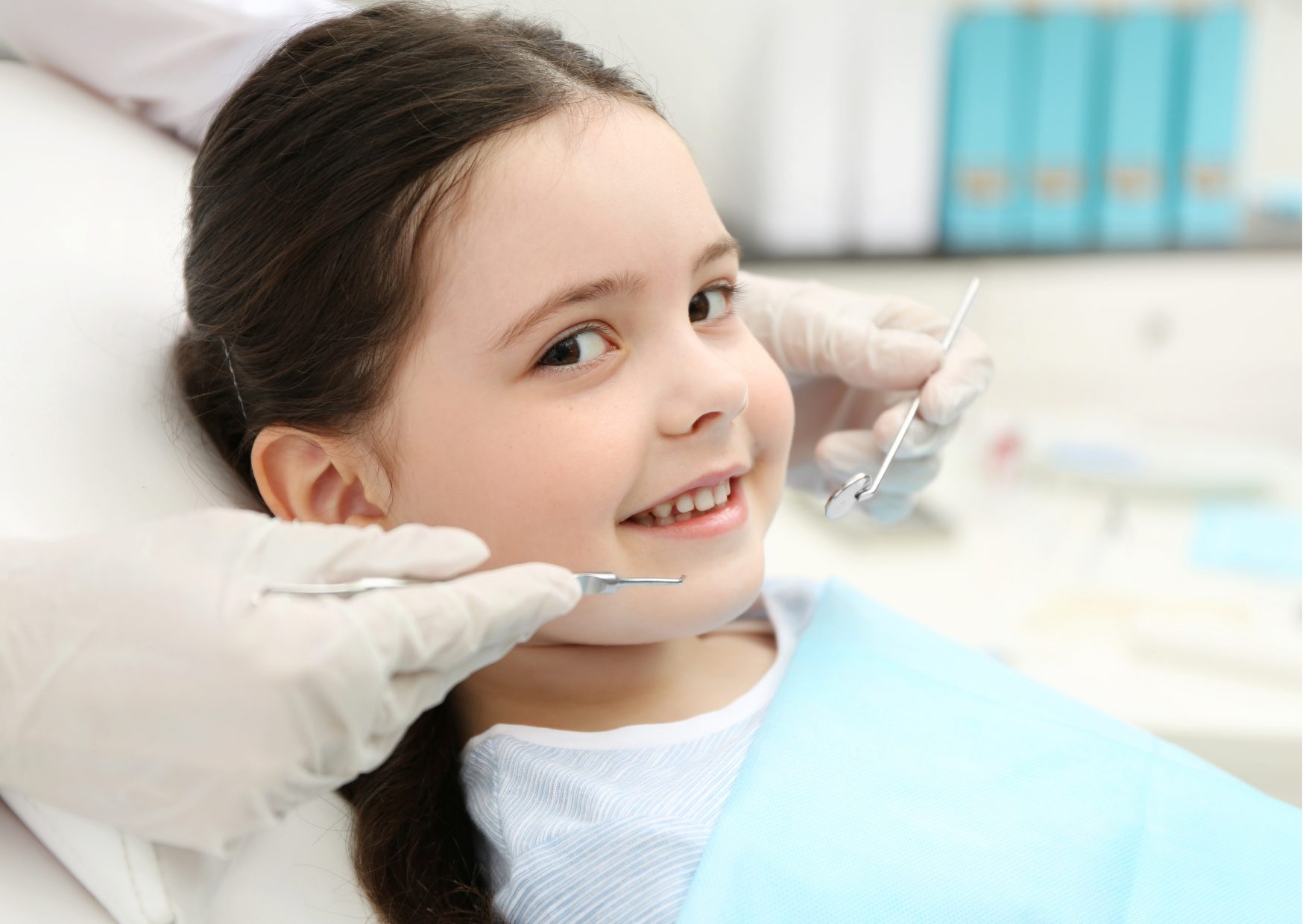 Niña de cabello oscuro sonríe a la cámara, sentada en el sillón dental.Tema: pulpectomía o endodoncia infantil de blog de Clínica Everest.