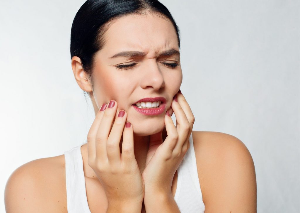 Mujer de pelo negro tomado, se toca la cara con evidente gesto de dolor. Tema: tipos de fractura dental del blog everest life