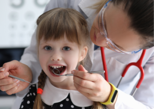 Odontopediatra mujer examina los dientes de una niña pequeña de trenzas .