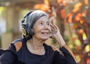 una anciana asiática escucha música con auriculares al aire libre. Tema: salud bucal y el alzhéimer para blog Everest Life