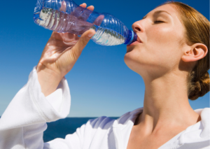 Mujer de perfil bebe una botella de agua con un fondo de cielo muy azul- Tema: sequedad bucal de Everest Life