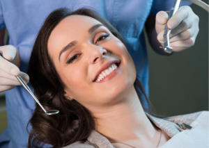 Joven mujer de cabello oscuro sonríe a la cámara mientras es atendida por el dentista. tema: prevención dental para el Blog Everest Life