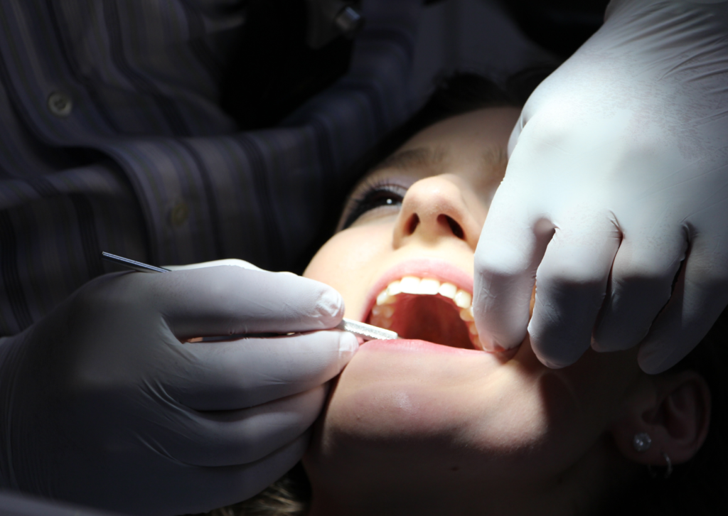 Imagen oscura, con la cara del paciente iluminada, mientras el odontólogo revisa su boca. tema: visitas regulares la dentista de Everest Life.