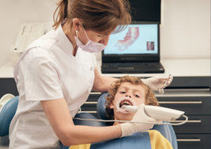 Vista lateral de una dentista que utiliza un escáner intraoral para un niño preadolescente para obtener moldes digitales dentales: Ortodoncia Moderna, para Everest Life.