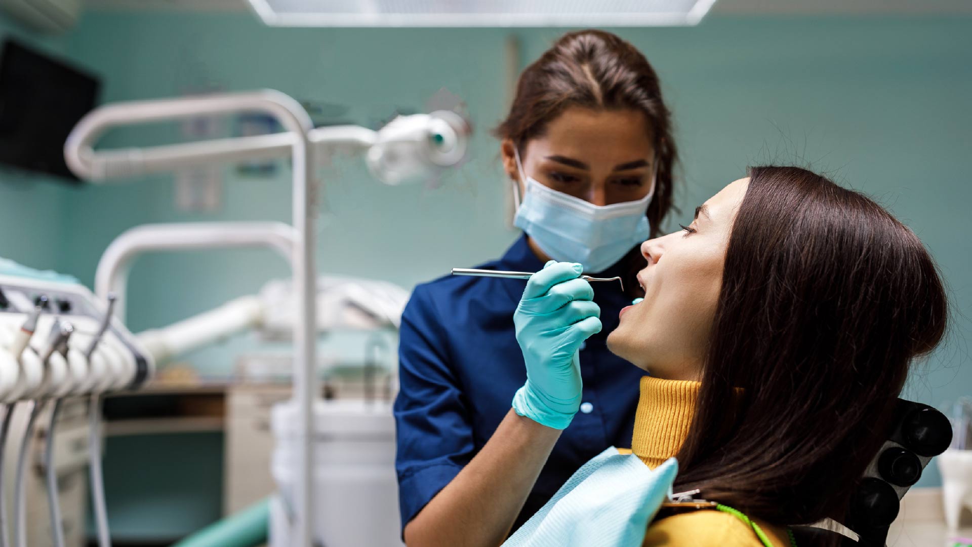 Dentista realiza una limpieza o higiene dental a una paciente. Usa guantes, mascarillas y sostiene una herramienta para remover el sarro.