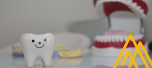 Maqueta de diente feliz guiña un ojo junto a una maqueta de boca. Contexto: errores comunes de salud dental: no ir al dentista